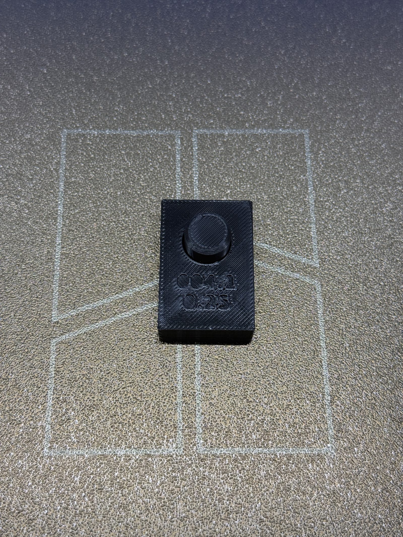 BRIM-004 iteration 1 assembled on the printer bed: the gauge block, debossed 004.1 and 0.25, seated flush on the peg plate, the dark PETG peg standing proud through the bore.