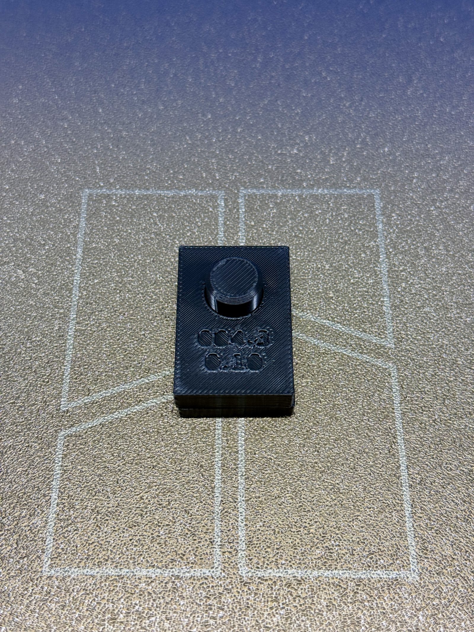 BRIM-004 iteration 3 assembled on the printer bed: the gauge block, debossed 004.3 and 0.10, seated on the peg plate with the dark PETG peg standing proud through the bore.